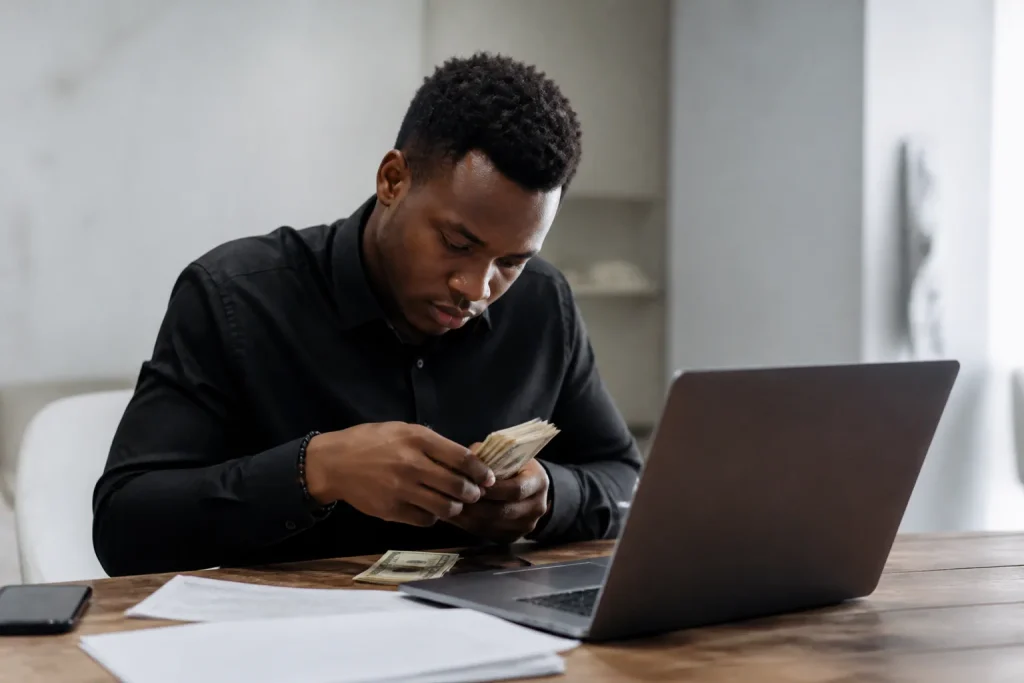 Jeune entrepreneur comptant des billets devant un ordinateur portable