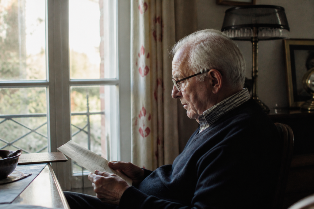Un senior assis devant une fenetre lit un courrier