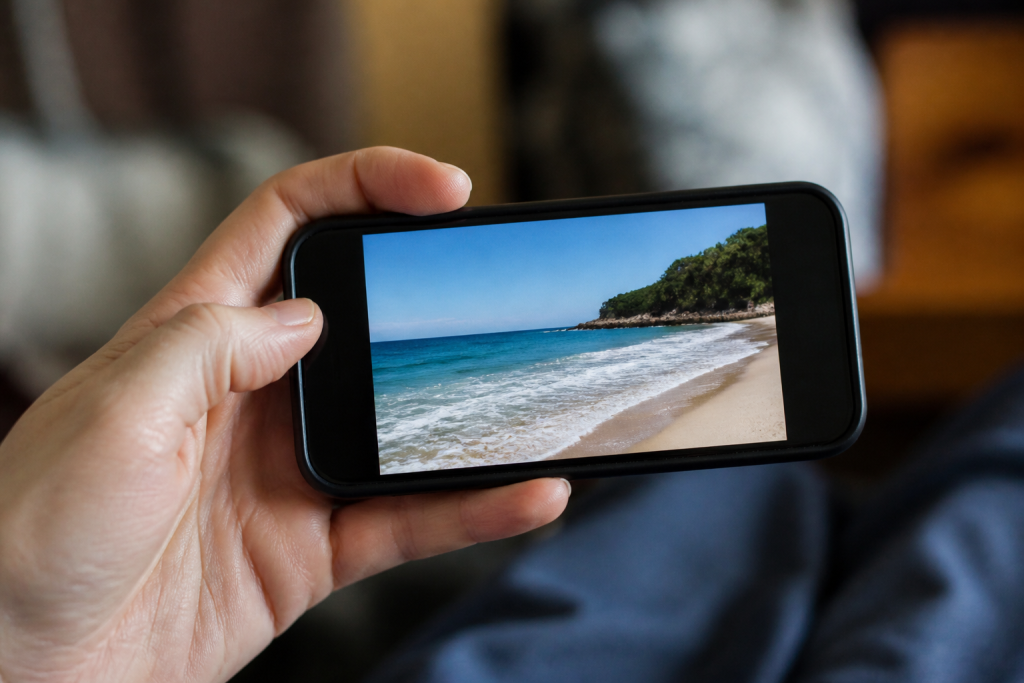 Main tenant un smartphone affichant une photo de plage